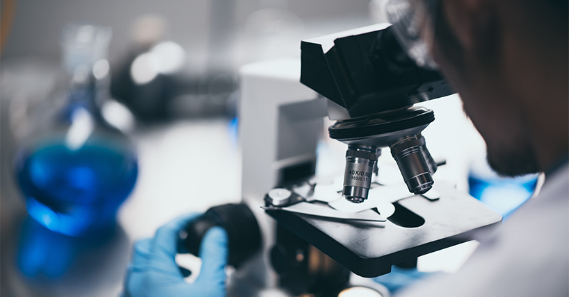 Microscope with blue gloved hands in a lab